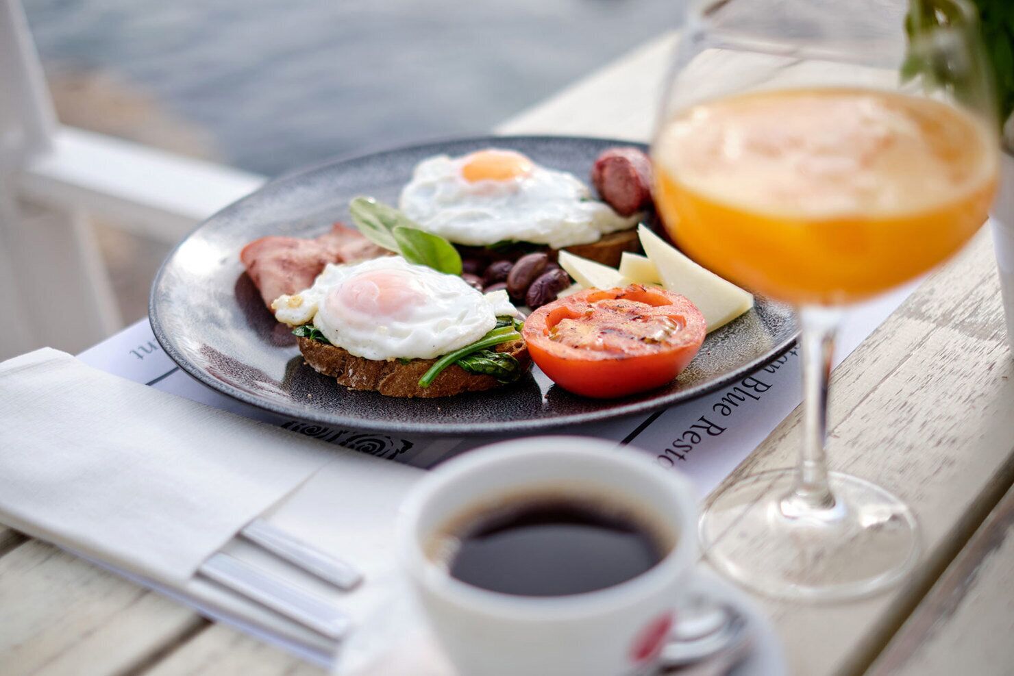 A breakfast plate with eggs, tomatoes, and greens, a glass of orange juice, and a cup of coffee on a wooden table.
