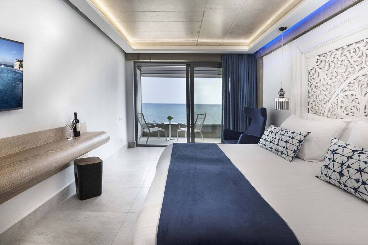 Een moderne hotelkamer met een groot bed, een zithoek met uitzicht op zee, een flatscreen-tv en een balkon met een glazen deur.
