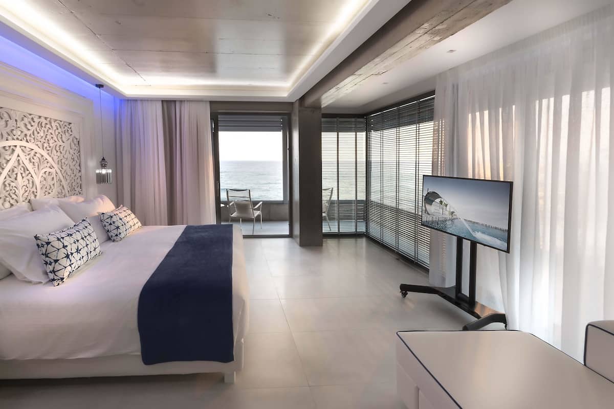 Een moderne hotelkamer met een groot bed, een televisie en een balkon met uitzicht op zee.