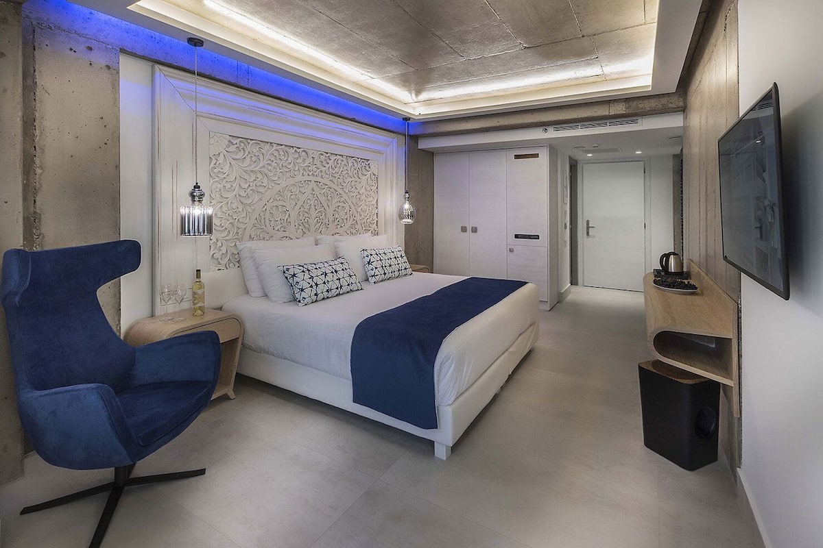 Een moderne hotelkamer met een bed, een blauwe stoel, een televisie en een minibar.