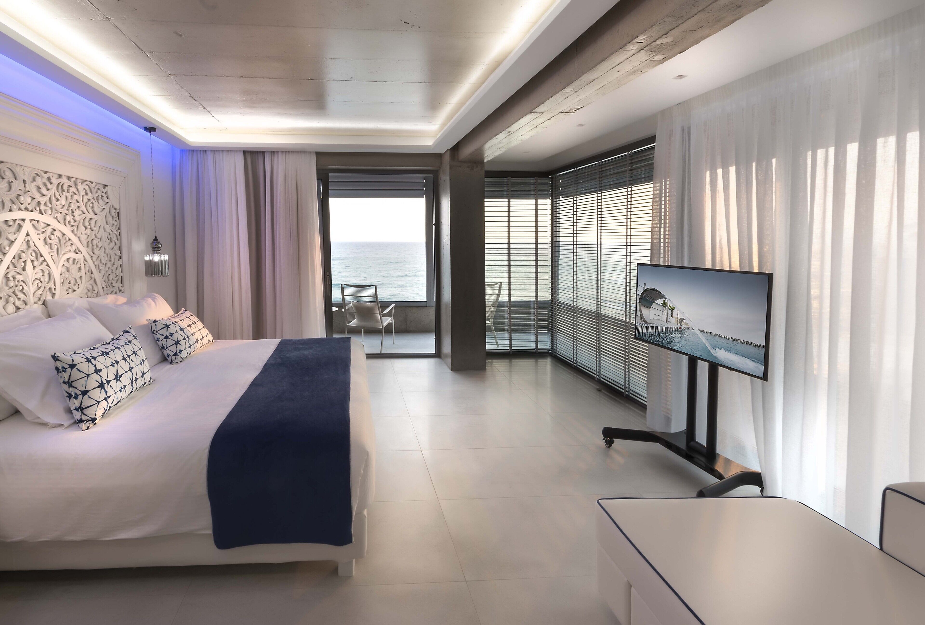 Quarto de hotel moderno com cama, televisão e varanda com vista para o mar.