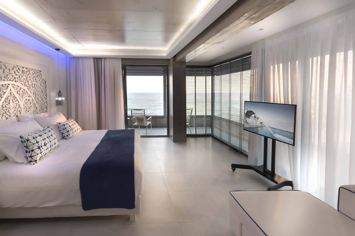 Een moderne hotelkamer met een bed, een televisie en een balkon met uitzicht op zee.