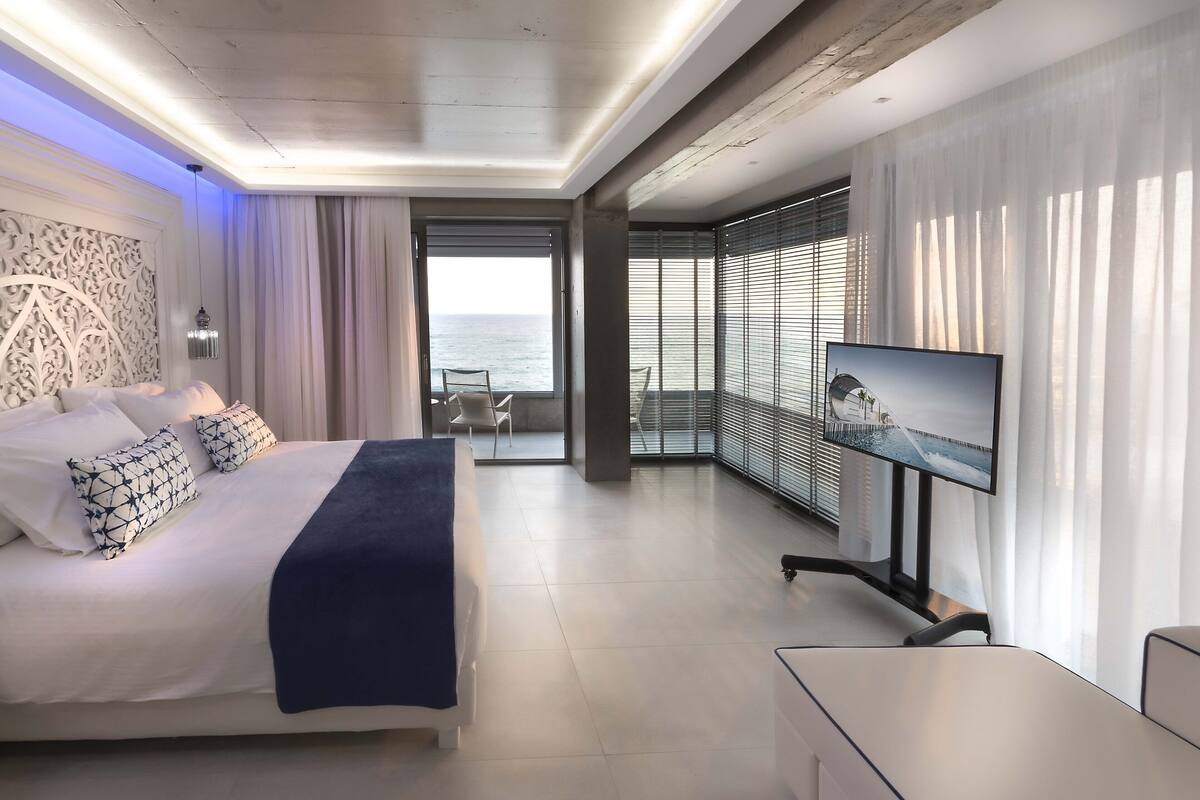 Quarto de hotel moderno com cama, televisão e varanda com vista para o mar.