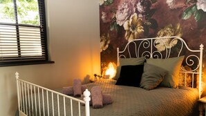 A bedroom with a bed, a window with blinds, and a floral wallpaper. - Romantic luxury apartment  great garden with fire table 5 minutes to the forest. (Wilbertoord)