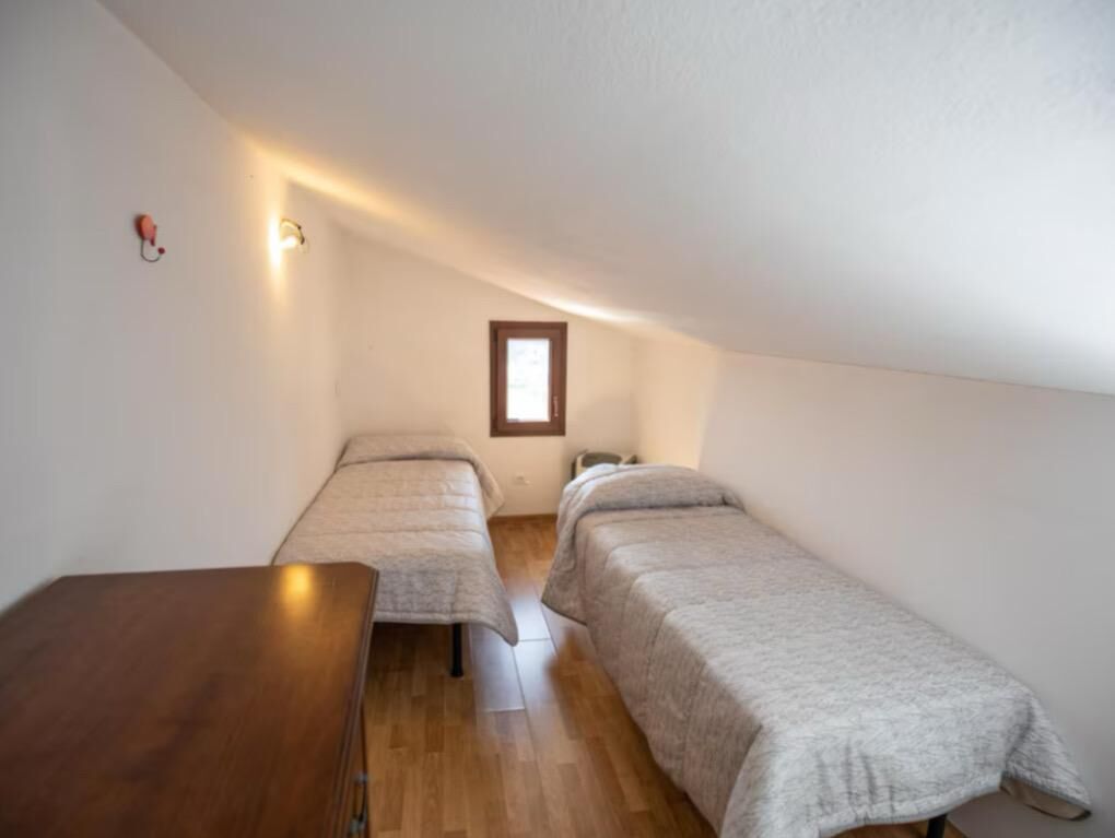 A small, dimly lit room with two single beds and a wooden table.