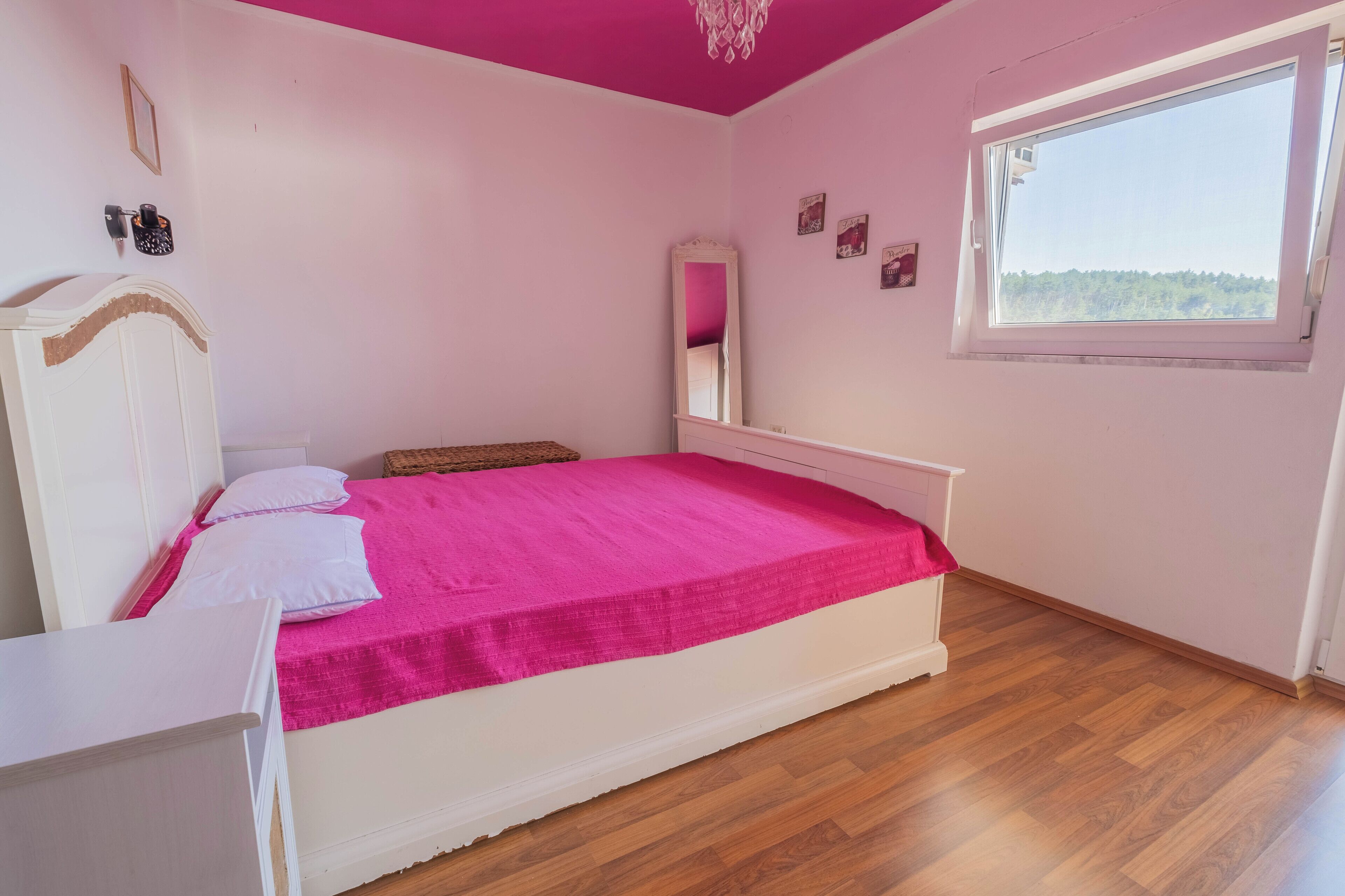 A bedroom with a bed, a bedside table, a dresser, a window, and a mirror.