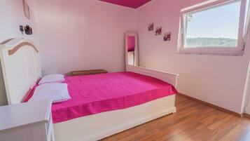 A bedroom with a bed, a bedside table, a dresser, a window, and a mirror.