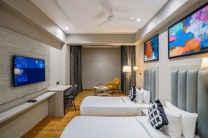 Hotellihuone, jossa on kaksi sänkyä, työpöytä, televisio ja taideteoksia seinillä.