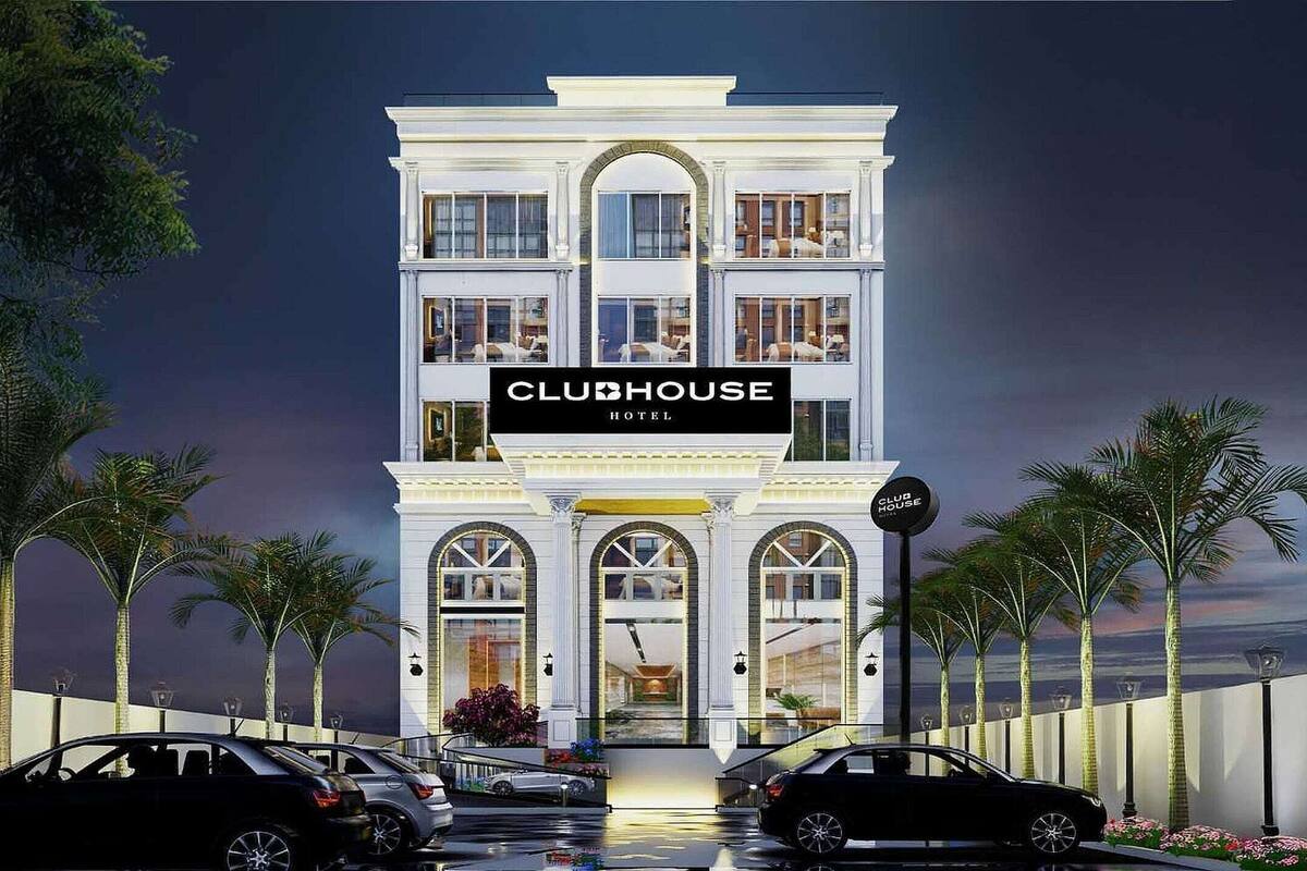Un hôtel à plusieurs étages, appelé CLUBHOUSE HOTEL, présente un style architectural classique, avec des fenêtres en arc et une entrée imposante.