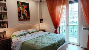 A bedroom with a large bed, a bookshelf, a painting, and a sliding glass door to a balcony. - Artemisia Apartment (VITERBO)