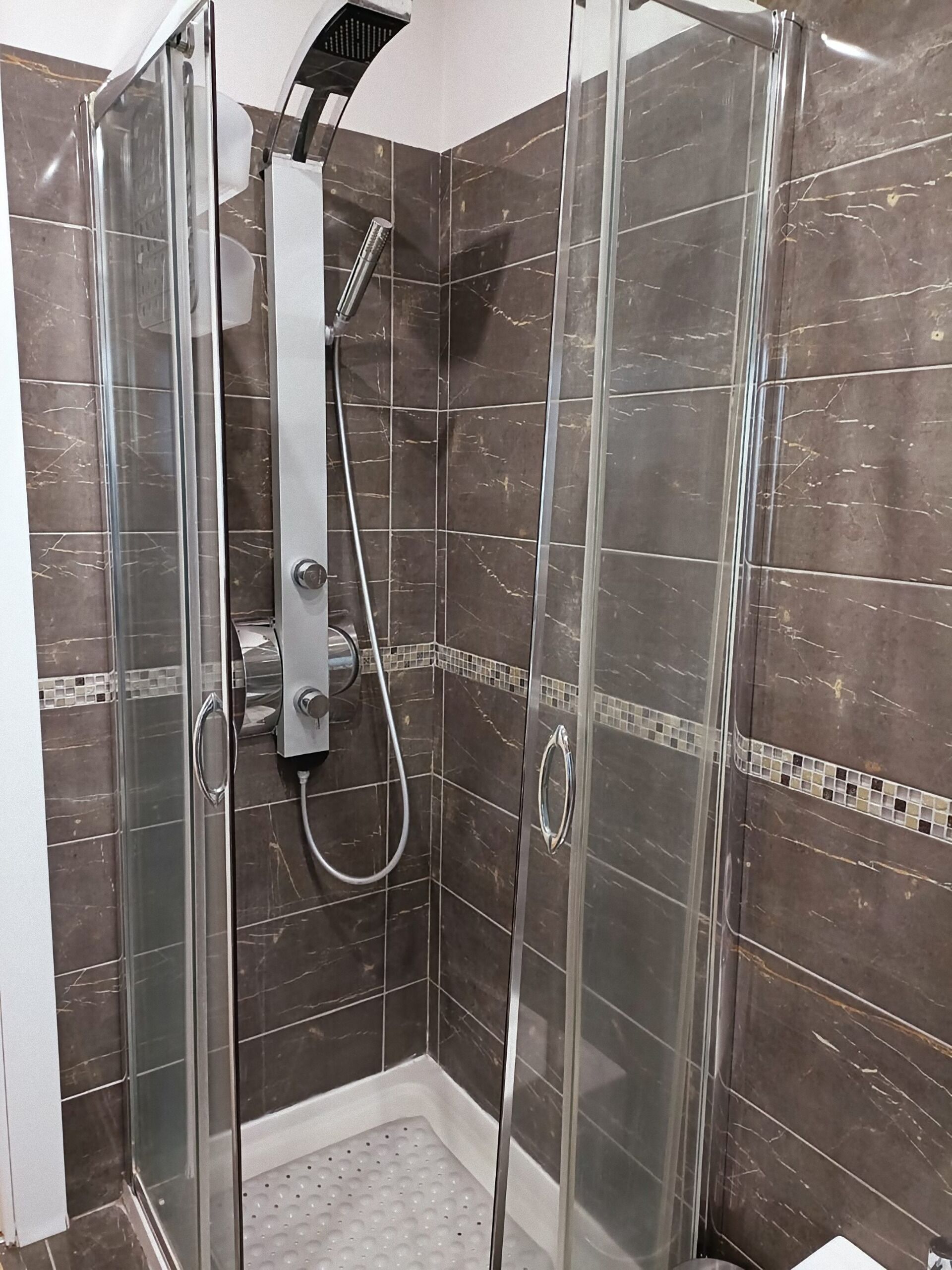 Una cabina doccia in vetro con soffione a mano e rubinetto a parete.