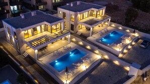 Ein moderner Wohnkomplex mit zwei Schwimmbecken, jedes umgeben von Liegestühlen und Terrassen, verbunden durch überdachte Gänge.