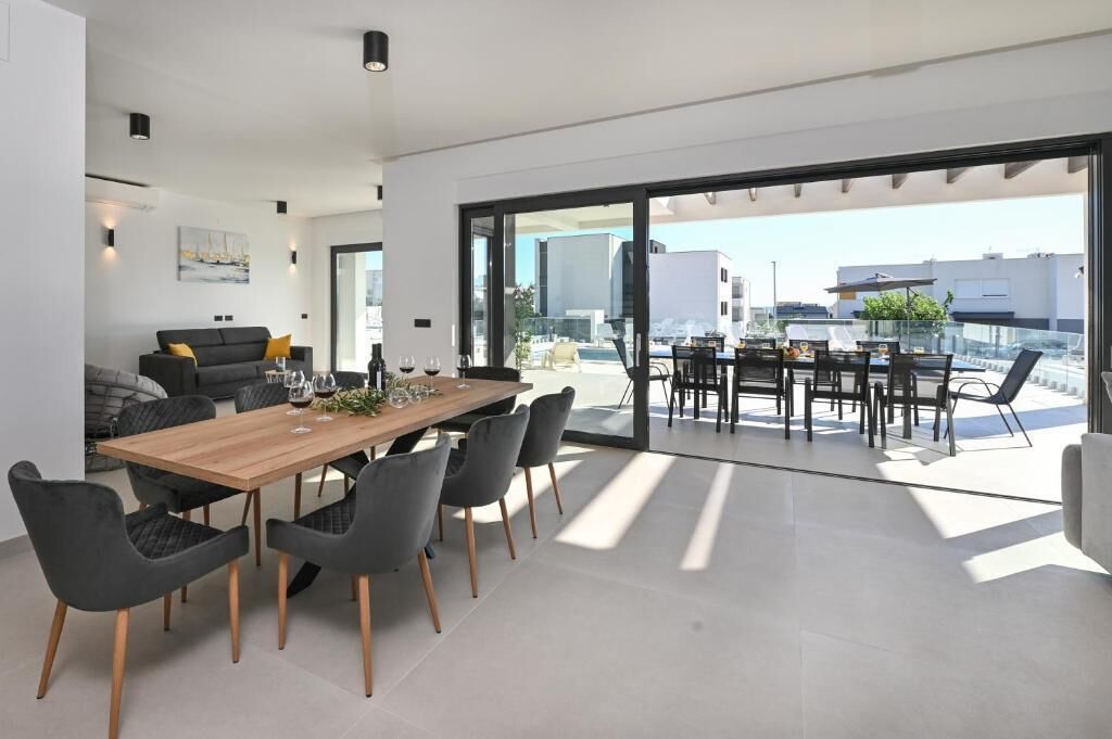 A modern dining area with a wooden table and chairs, a sofa, and a view of the city through large glass doors.
