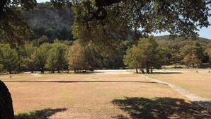 Um parque com áreas gramadas, árvores e uma montanha ao fundo.
