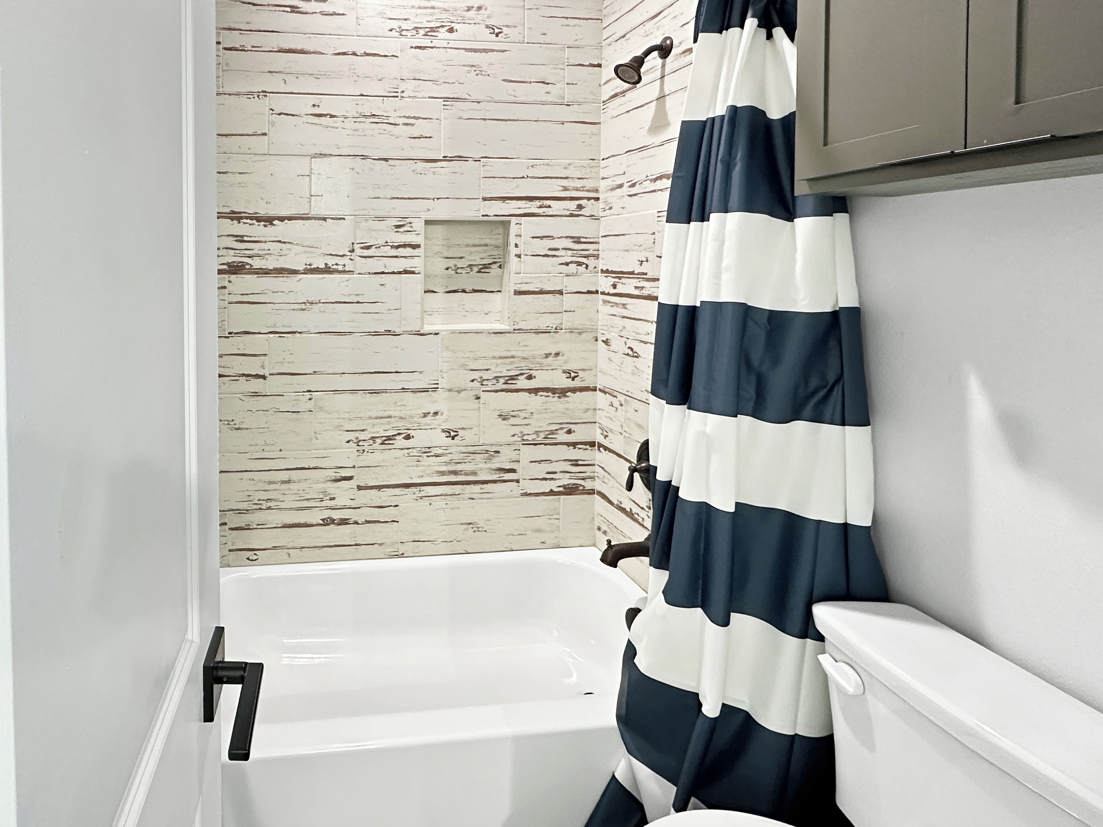 A bathroom with a white bathtub, a shower curtain, and a wall with a distressed wood texture.