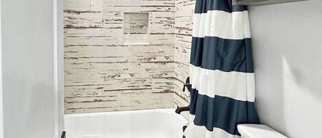 A bathroom with a white bathtub, a shower curtain, and a wall with a distressed wood texture.