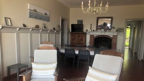 A living room with two upholstered chairs, a fireplace, a dining table, and a TV.