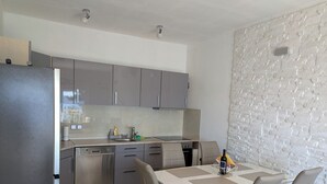 A modern kitchen with grey cabinets, a built-in oven, and a dining area with a table and chairs. - Breladreams Apartment *** (Brela)