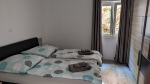 A bedroom with two beds, each with a patterned duvet and pillows, a wooden headboard, and a window with curtains. - Breladreams Apartment *** (Brela)