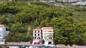 A residential area with two-story buildings, a paved road, and a hillside with dense greenery. - Breladreams Apartment *** (Brela)