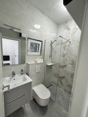 A modern bathroom with a sink, toilet, and glass-enclosed shower. - Breladreams Apartment *** (Brela)