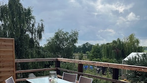 A wooden deck with a glass table and chairs, surrounded by a wooden railing.