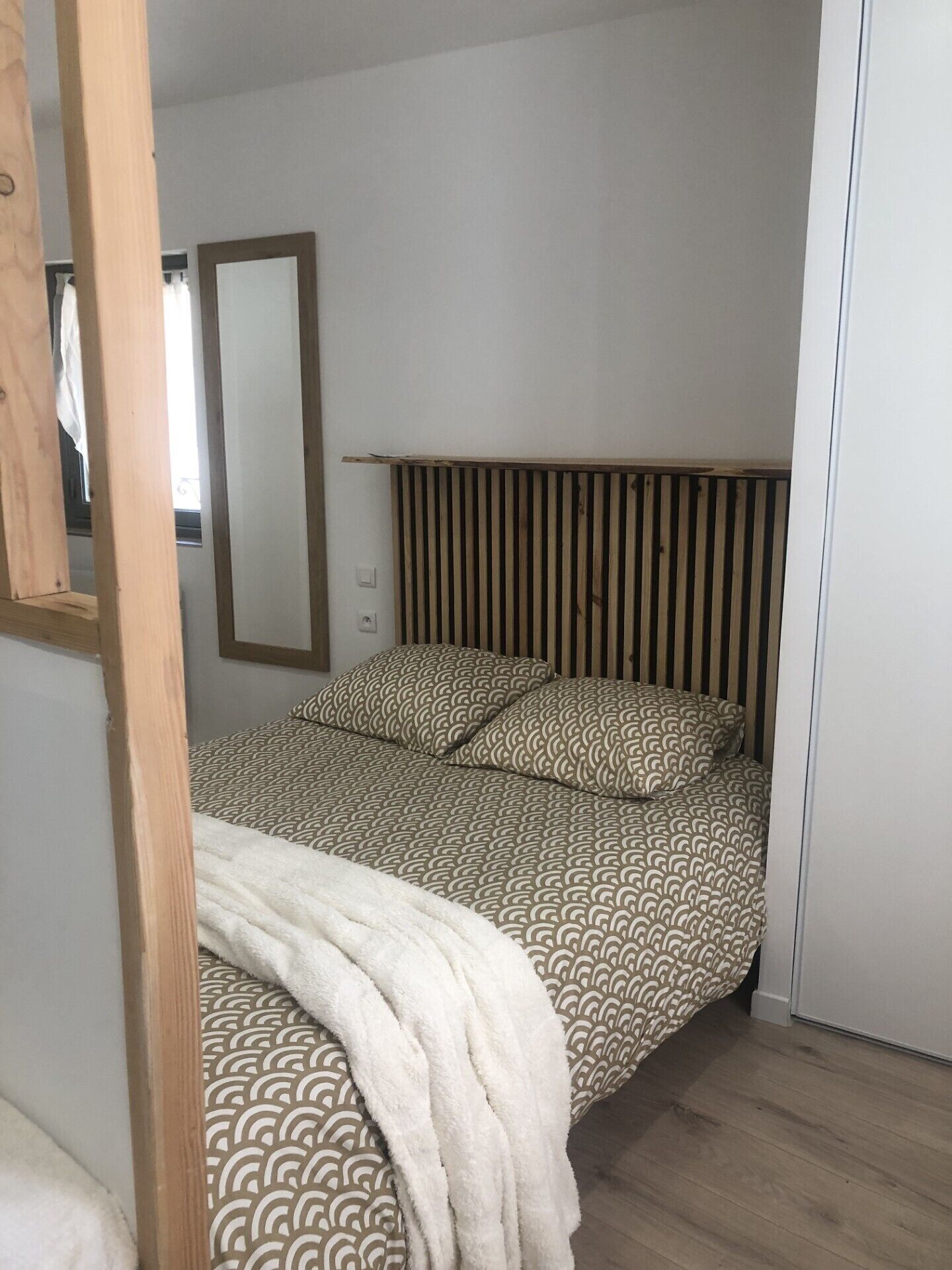 A bedroom with a bed, a wooden headboard, a mirror, and a white wall.