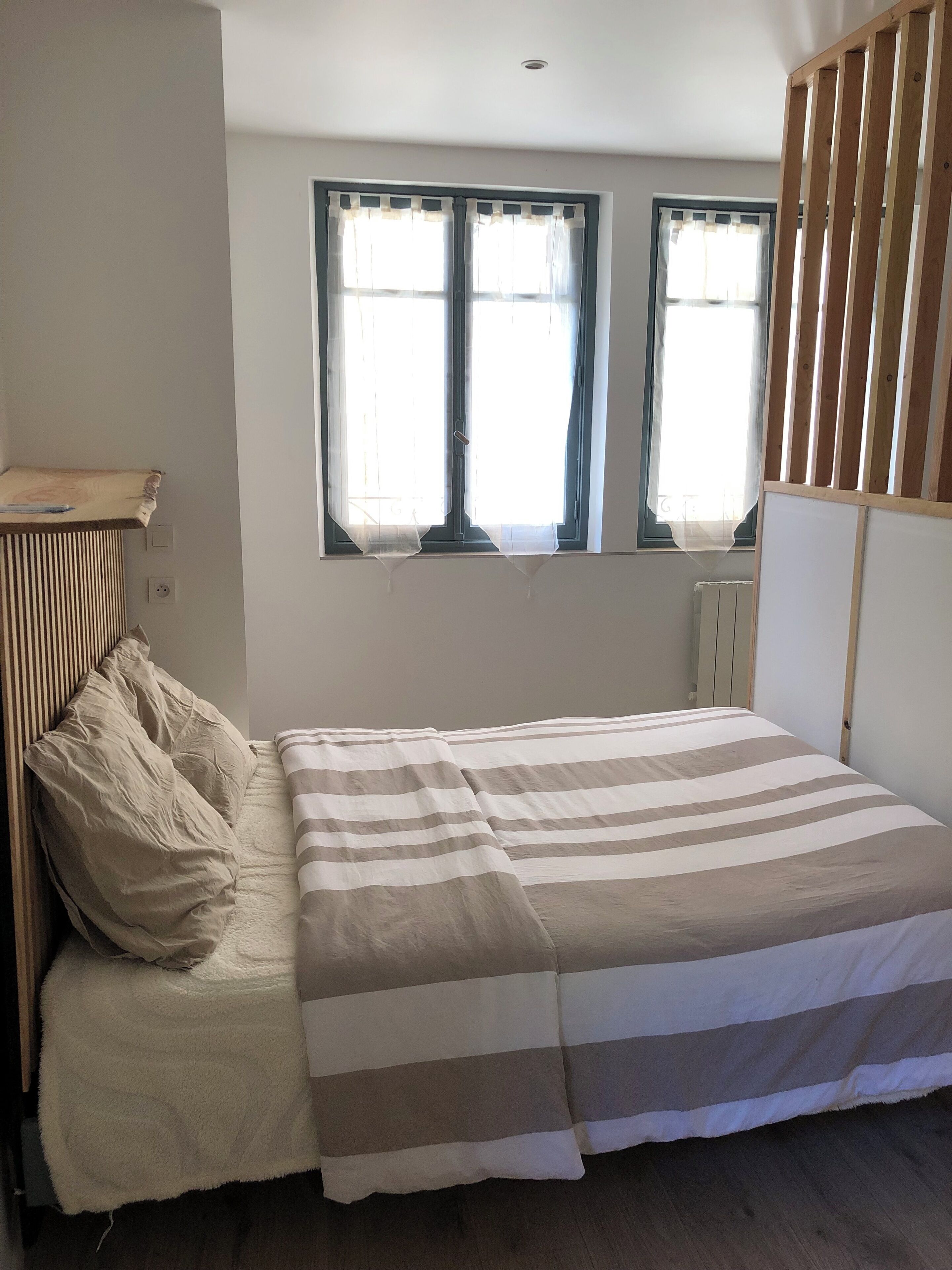 Une chambre à coucher avec un lit, une fenêtre avec des rideaux, un radiateur et une tête de lit en bois.