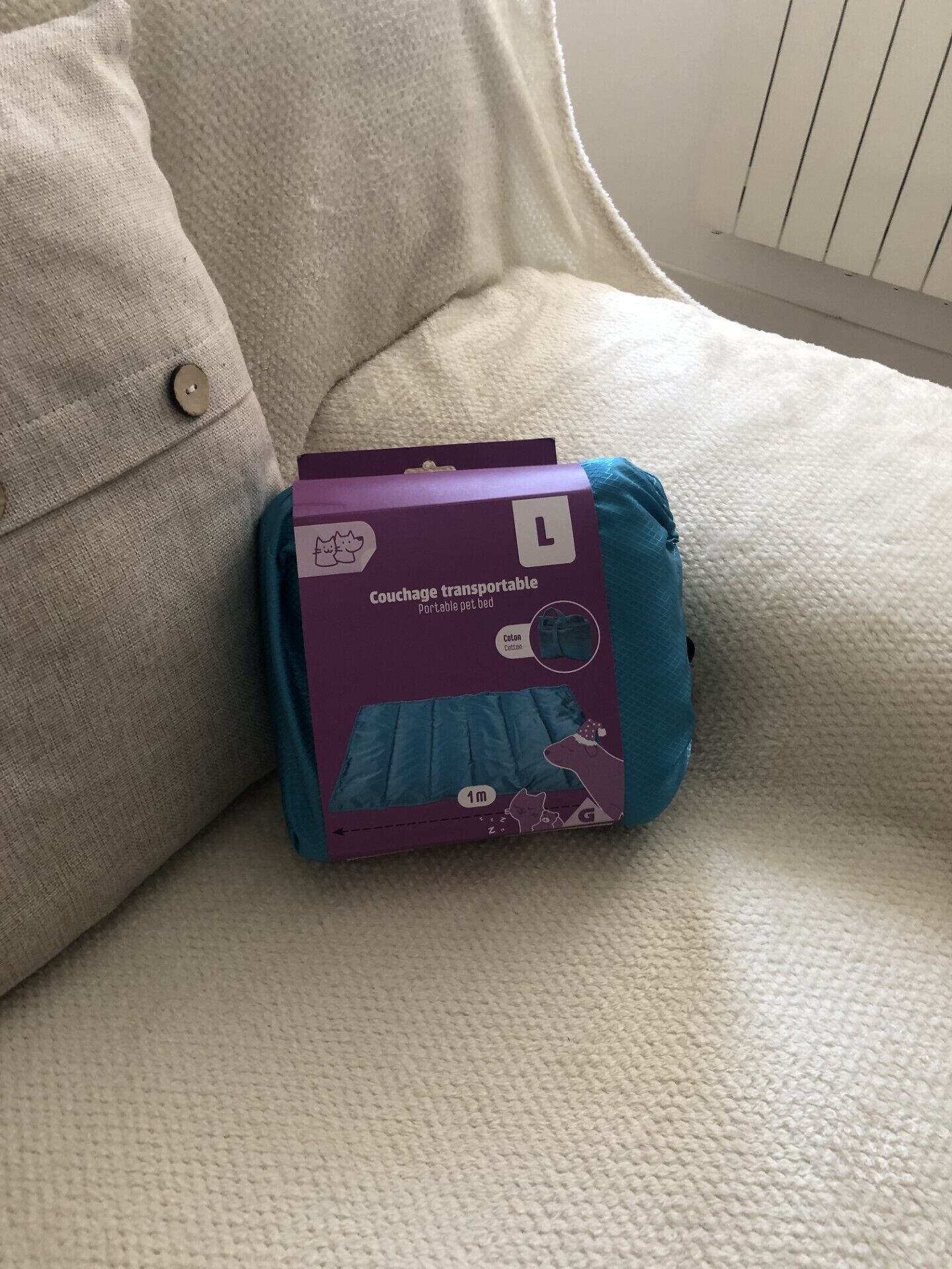 Eine violette Kiste mit dem Aufdruck 'Couchage transportable' auf einem beigen Sofa.