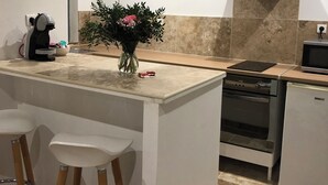 Een kleine keuken met een centraal eiland, barkrukken, een inbouwoven en een vaatwasser.