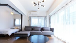 A modern living room with a sectional sofa, a round coffee table, and a large window with curtains. - Creare Togoshi Ginza by Tranova (Tokyo)