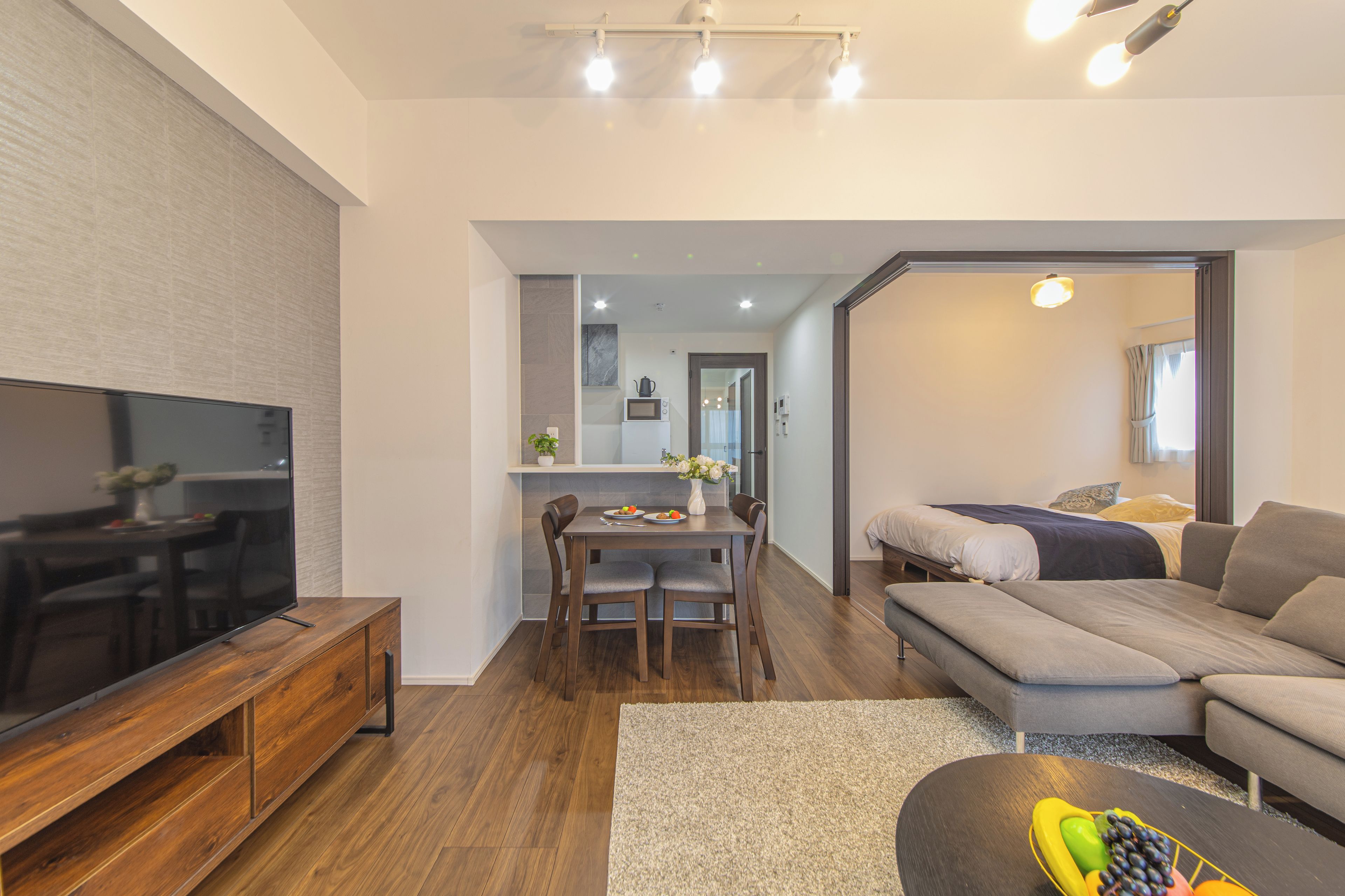 Una sala de estar moderna con un televisor de pantalla plana, un sofá, un comedor con mesa y sillas, y una cocina al fondo.