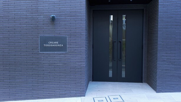 A modern building entrance with a dark brick facade, a sign reading 'CREARE TOGOSHIGINZA,' and a double door with glass panels. - Creare Togoshi Ginza by Tranova (Tokyo)