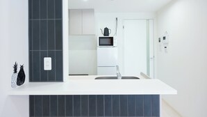 A modern kitchen with a white countertop, dark tiles, a microwave, and a sink. - Creare Togoshi Ginza by Tranova (Tokyo)