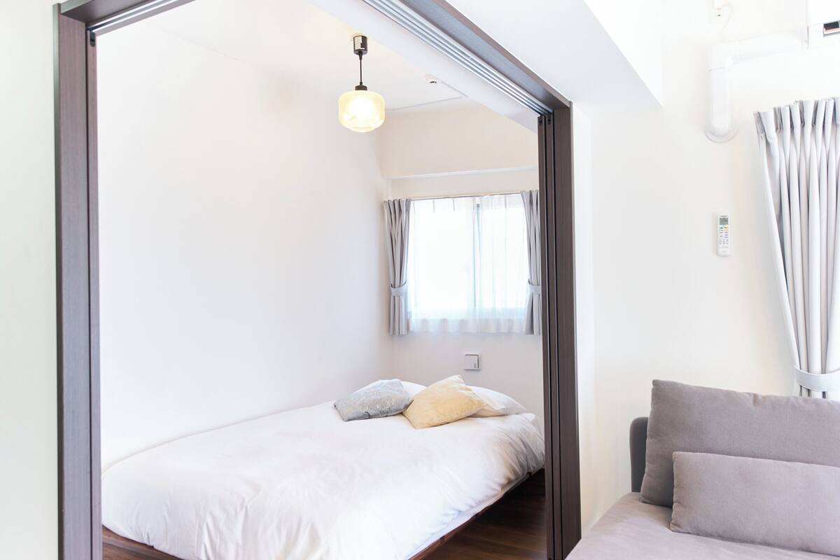 A bedroom with a bed, a bedside table, a lamp, a window with curtains, and a view of the outside.