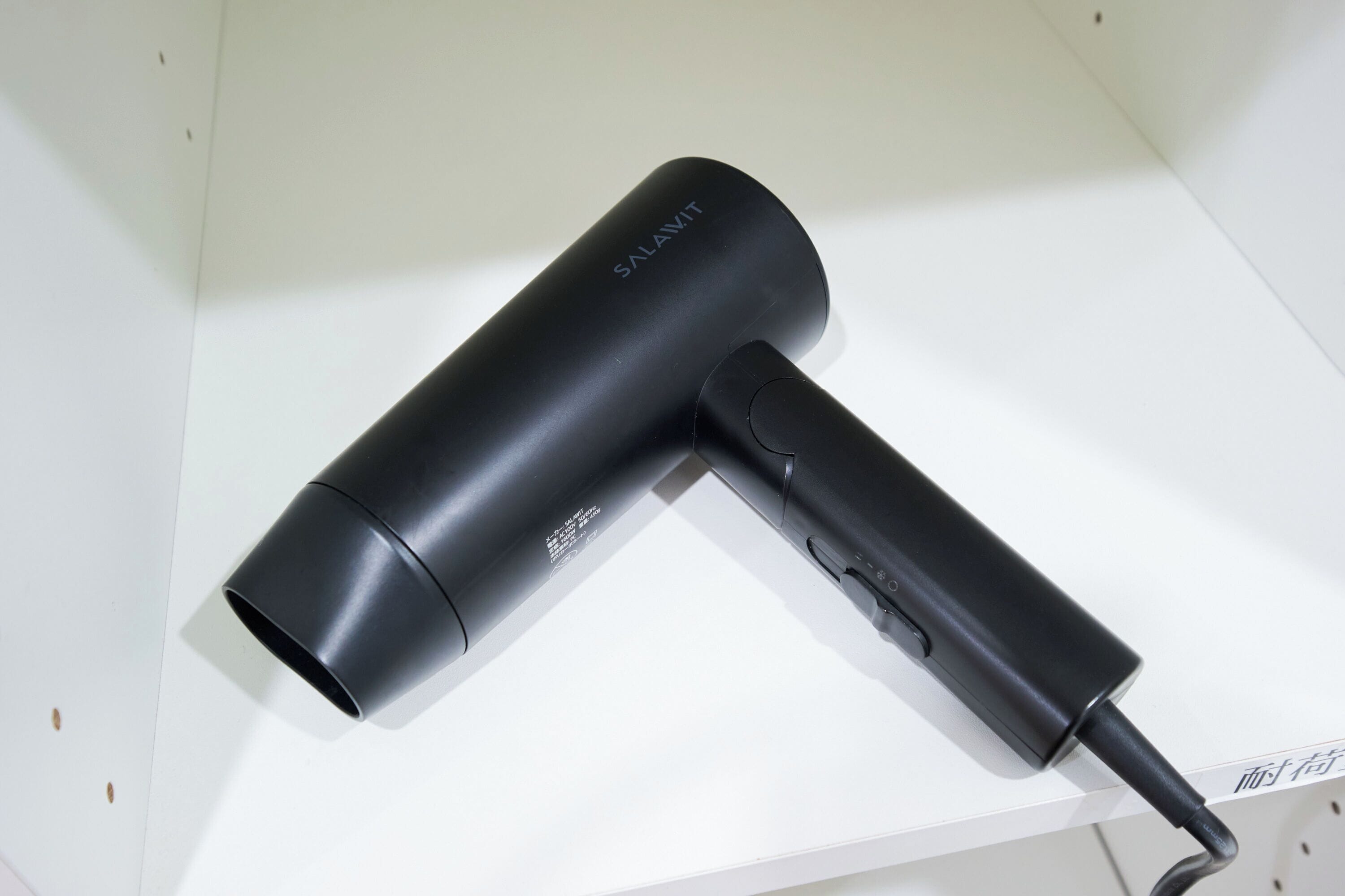 A black hairdryer with the brand name 'SALAVIT' on a white shelf.