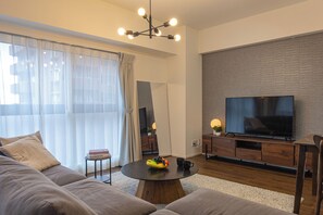 A modern living room with a sofa, a coffee table, a TV, and a dining area. - Creare Togoshi Ginza by Tranova (Tokyo)