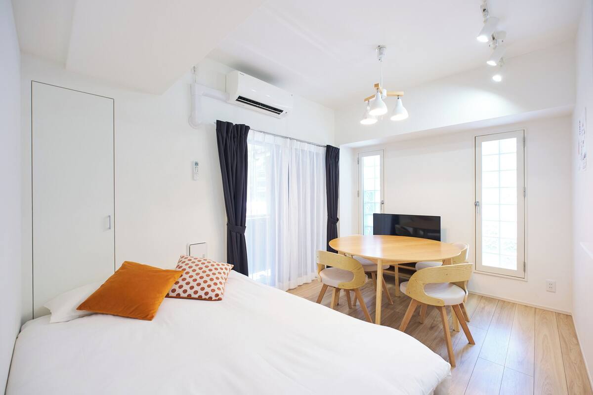 A bedroom with a bed, a dining table with chairs, an air conditioning unit, and a television.