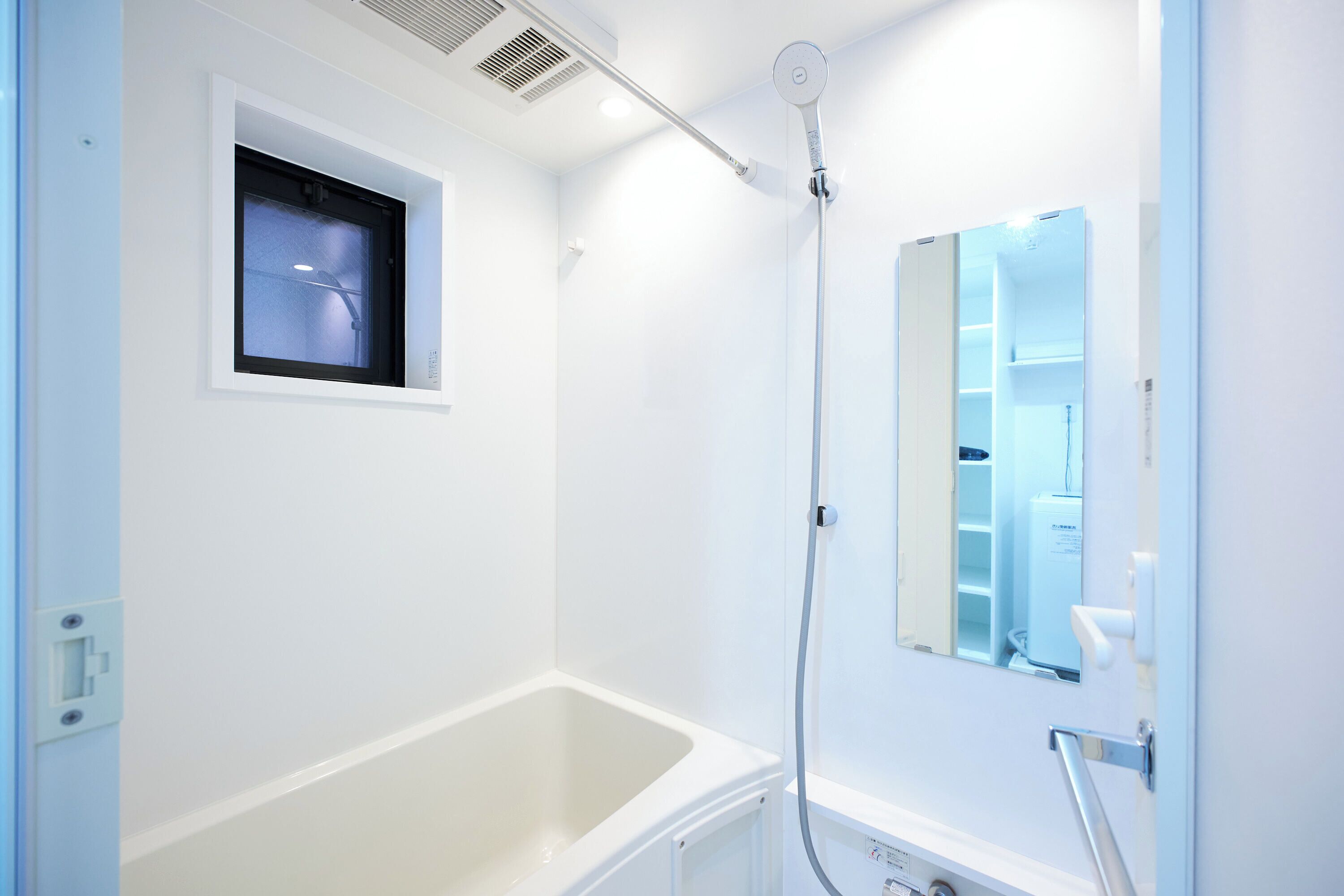 A modern bathroom with a white bathtub, a shower with a handheld showerhead, a small window, and a mirror.