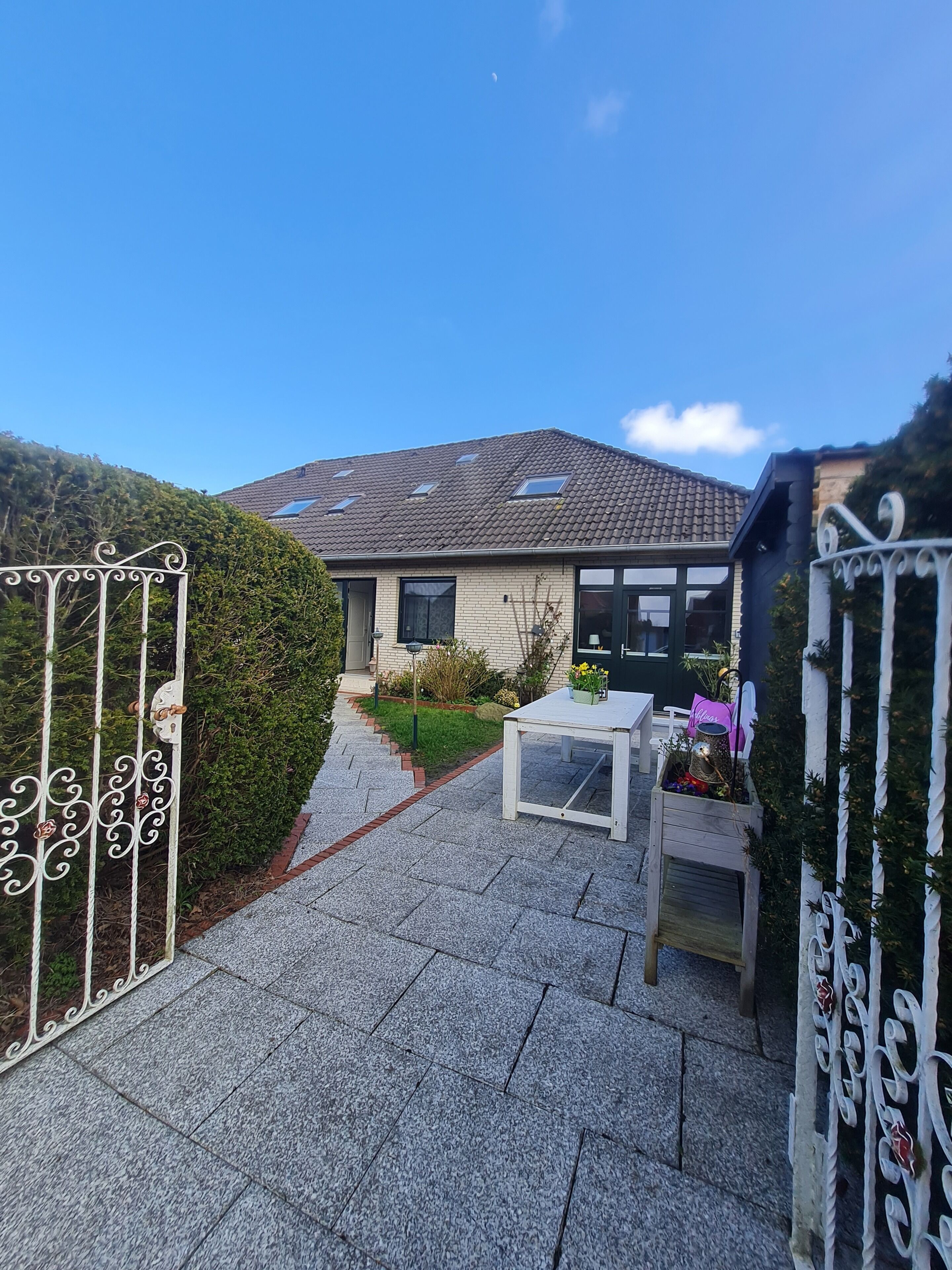 A house with a tiled roof, a front garden, a white table, and a decorative gate.