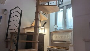 A spiral staircase with a wooden finish, a small table, and a radiator in a room with a tiled floor. - Charming 1-bedroom house in adorable Putignano with WiFi, AC (Putignano)
