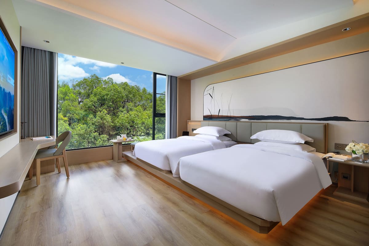 Una habitación de hotel moderna con dos camas, un escritorio y un ventanal con vistas a árboles.