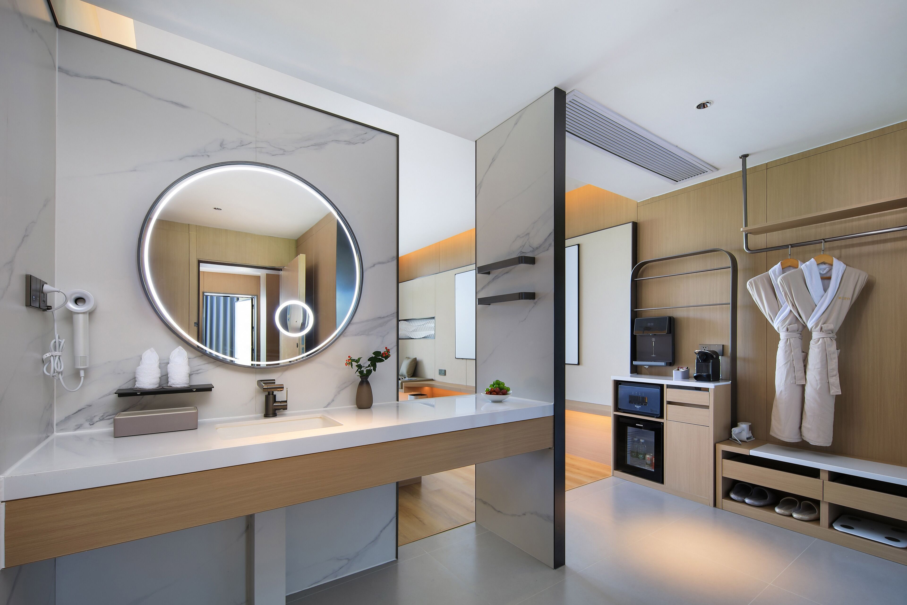 Een moderne badkamer met een marmeren wastafel, een ronde spiegel, een ingebouwde verwarming en een badjas ophangrek.