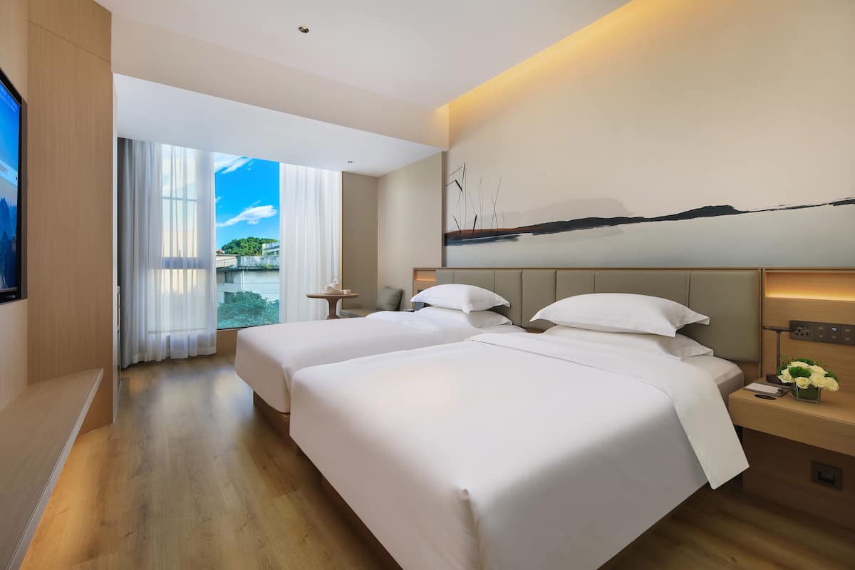 Una habitación de hotel moderna con dos camas, un televisor, un cuadro y vistas a zonas verdes.