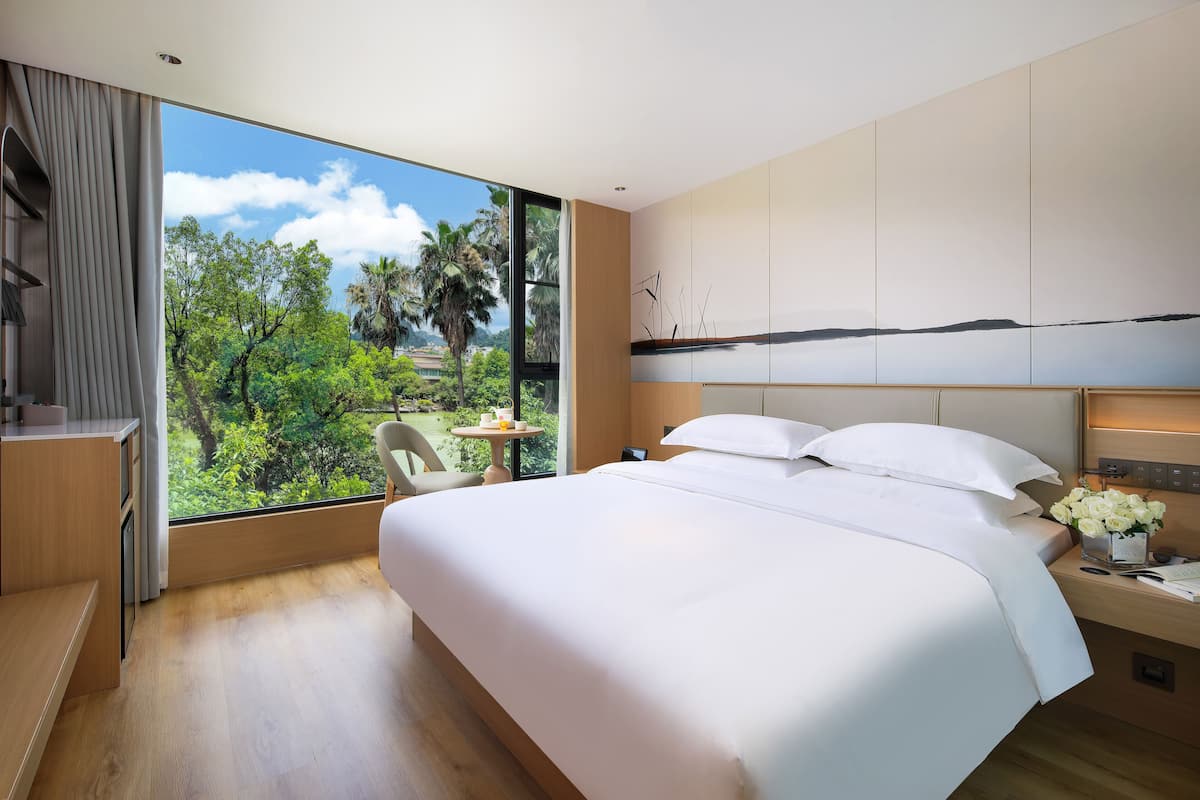 Una habitación de hotel moderna con una cama grande, un escritorio y vistas a vegetación exuberante.