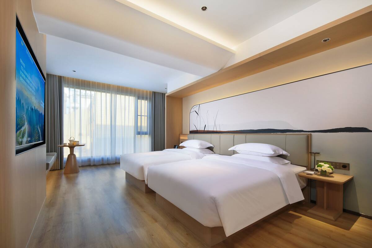 Habitación de hotel con dos camas, un escritorio, un televisor y un ventanal con cortinas.