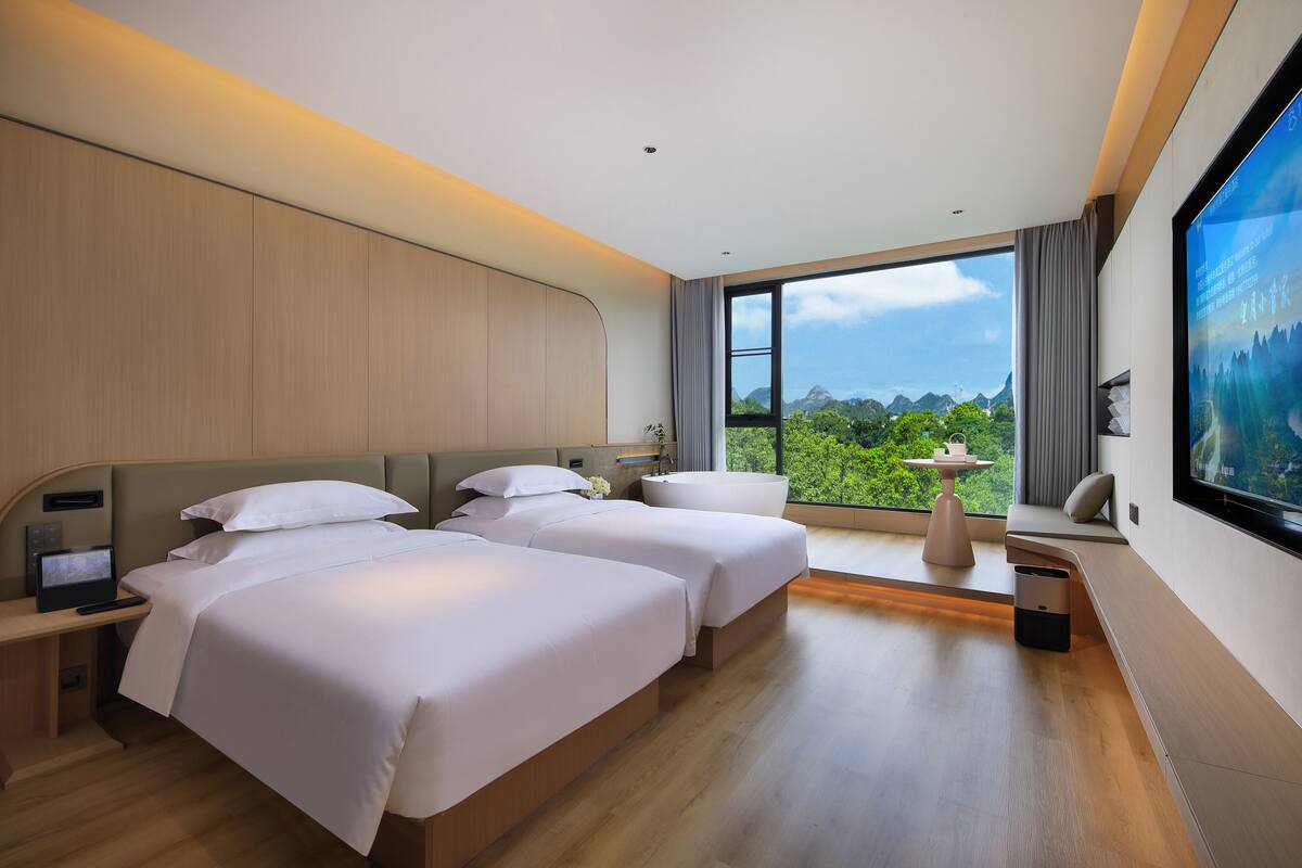 Habitación de hotel moderna con dos camas, un escritorio, un televisor y un ventanal con vistas al exterior.