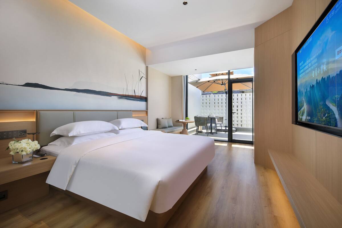 Una habitación de hotel moderna con una cama grande, un televisor y un balcón con vistas.