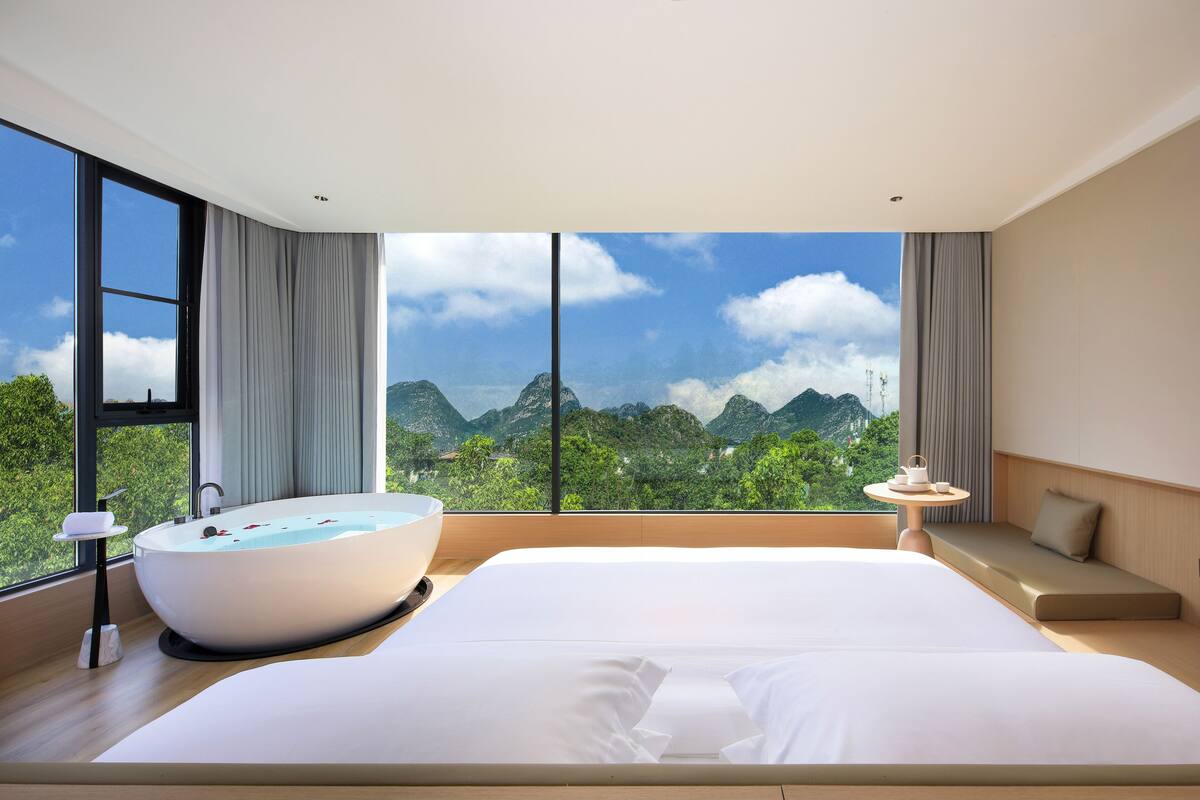 Una habitación de hotel moderna con una cama grande, una bañera y vistas a las montañas.