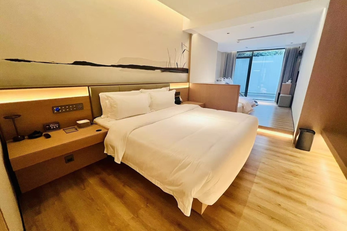 Una habitación de hotel moderna con una cama grande, mesitas de noche, un panel de control y vistas al balcón.